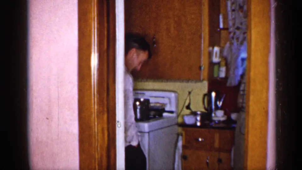 1955 New York home interior showing a man partly visible in a doorway beside a white stove and wood cabinets.