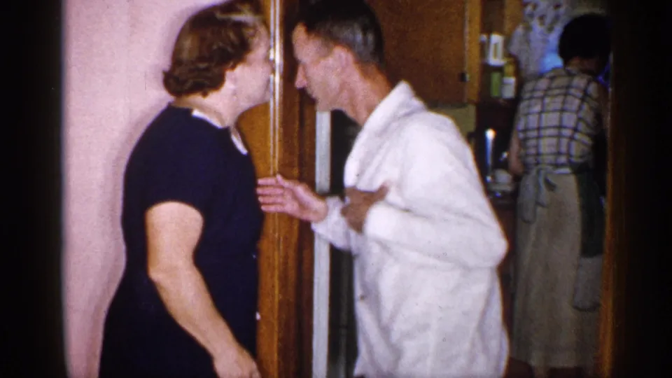 1955 New York frame showing two adults close together at a kitchen doorway with another person partly visible in the background.