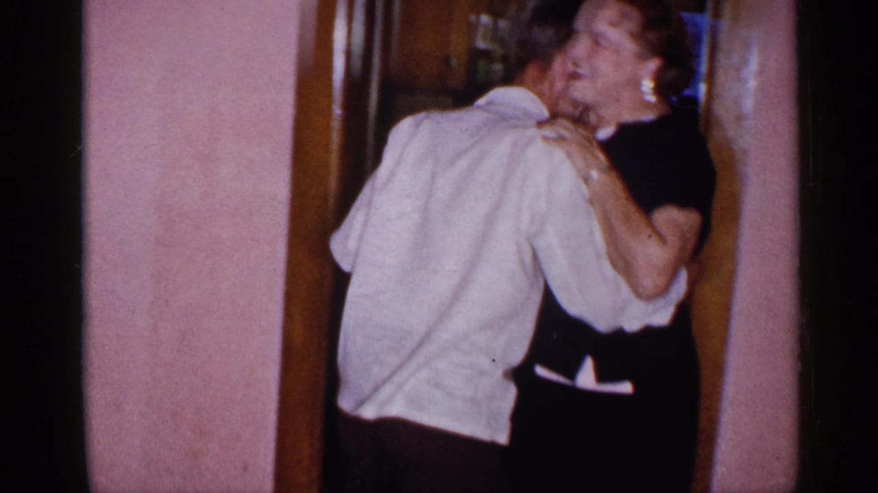 Man and woman embracing in a doorway beside pink interior walls.