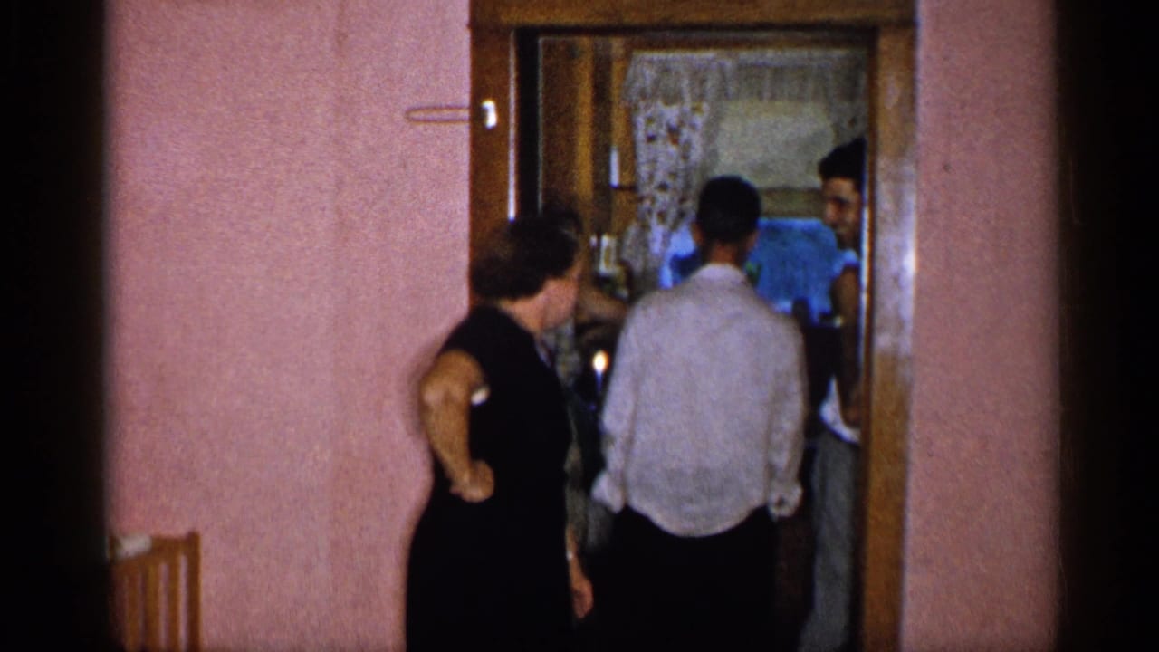 Woman in a black dress watches a man pass through a doorway in a home interior.