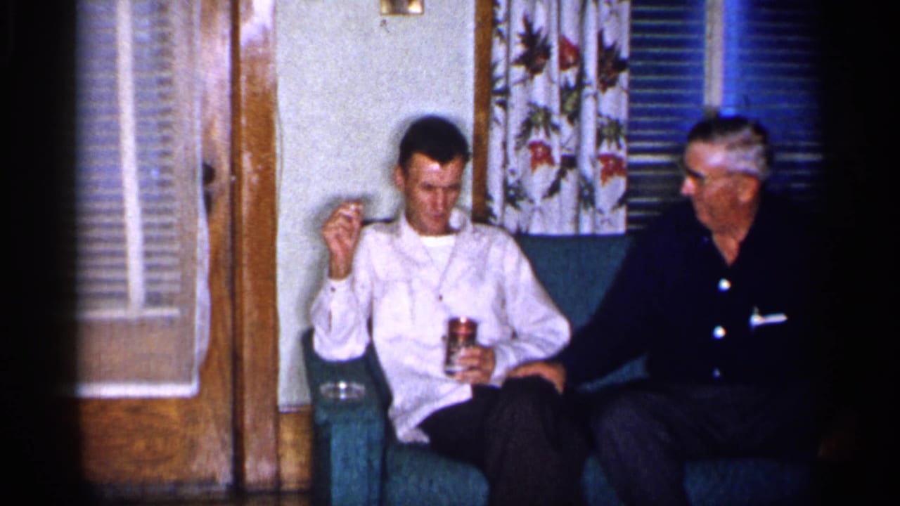 Two men remain seated on a teal couch, with a can and cigarette visible.