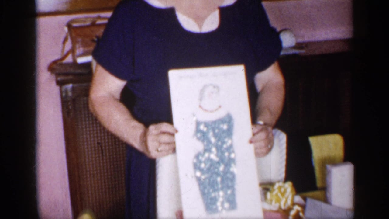 Woman in a navy dress holds a framed illustration in a living room.