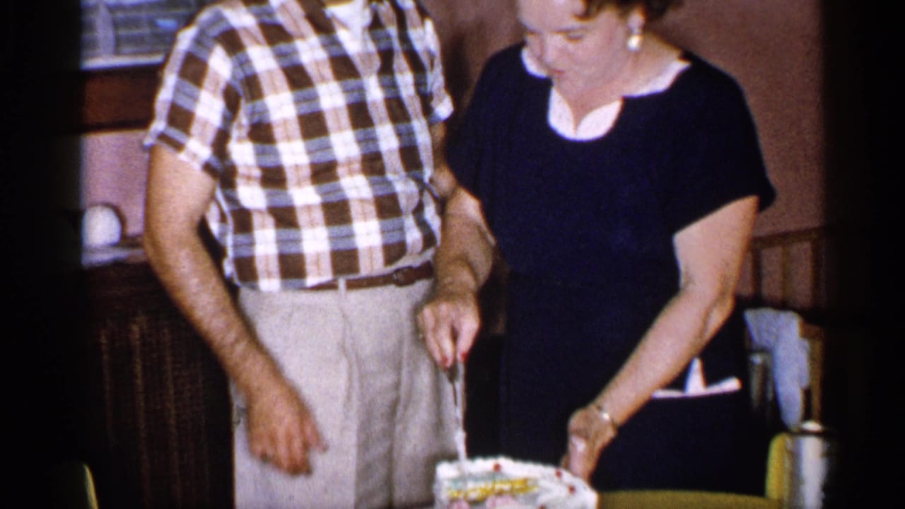 Man and woman stand beside a frosted cake as the woman holds a knife.