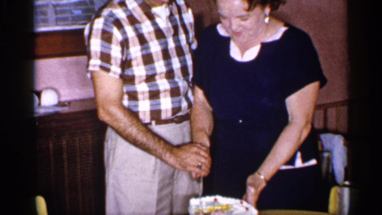 The couple holds the knife together over a decorated cake indoors.