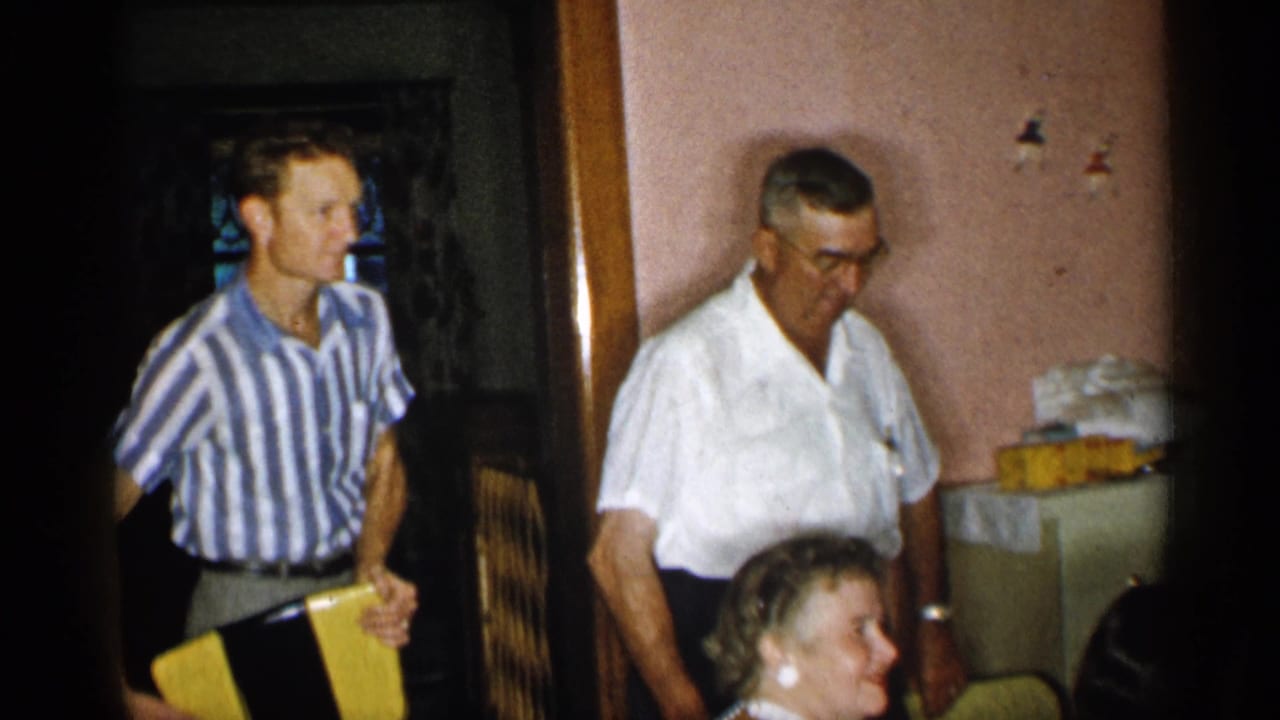 A man in a striped shirt holds a yellow object while another man in a white shirt stands nearby.