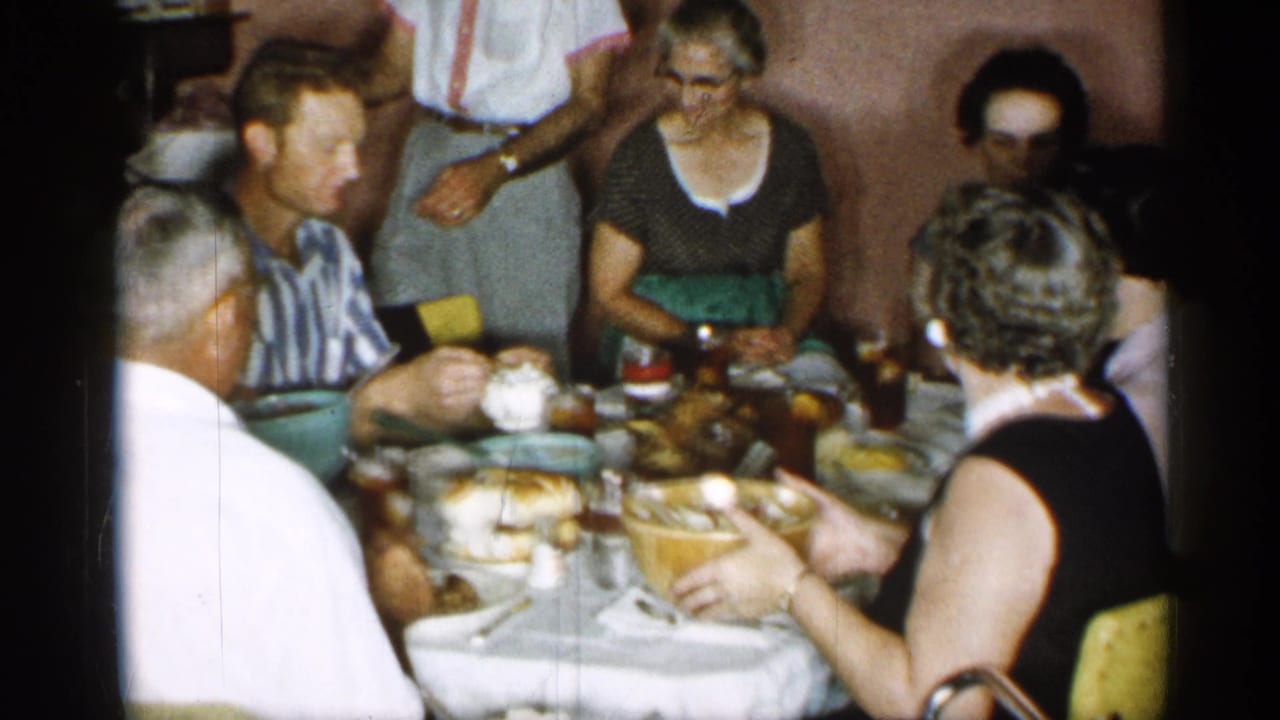 Adults seated around a dining table with plates, bowls, glasses, and food being served.