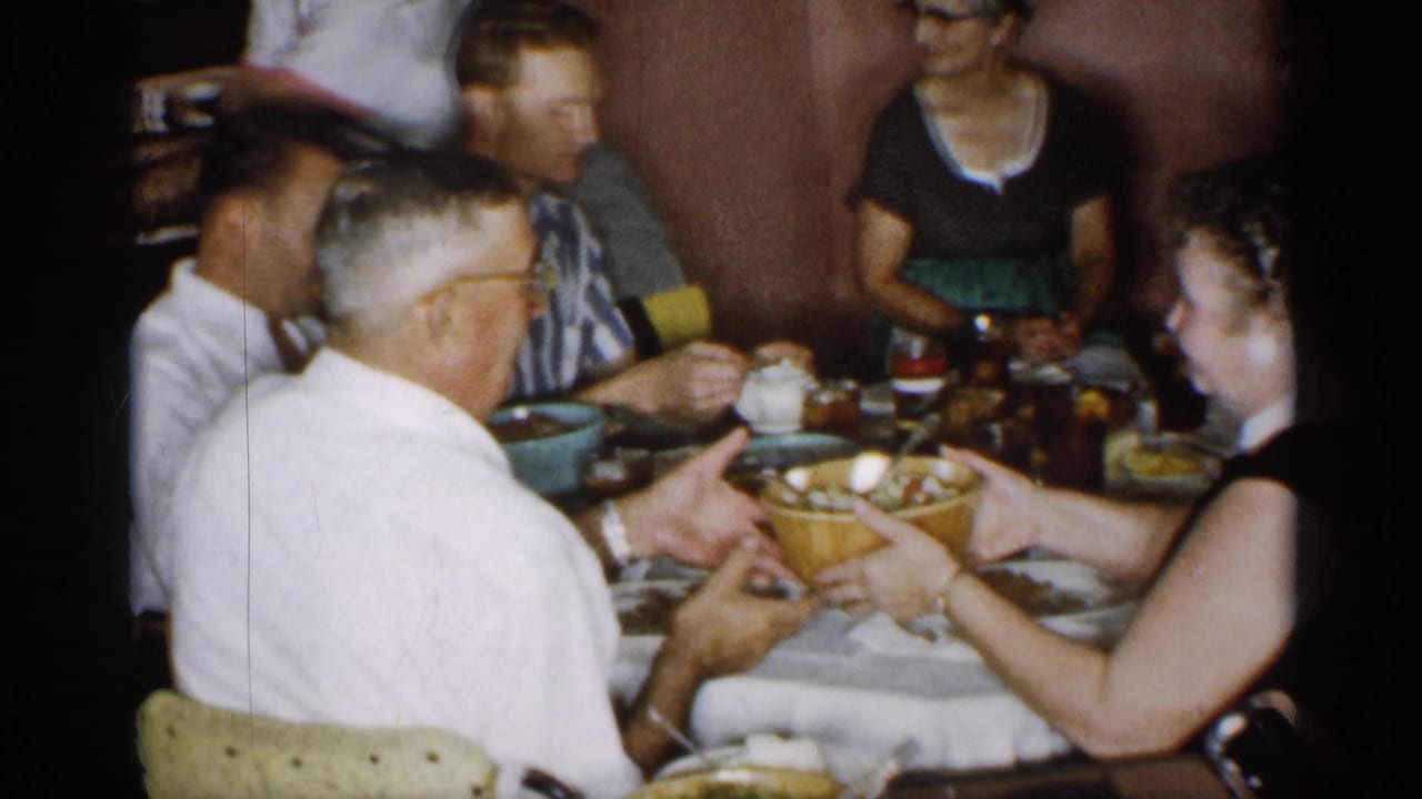 Adults at a dinner table pass a large bowl while seated in a home interior.