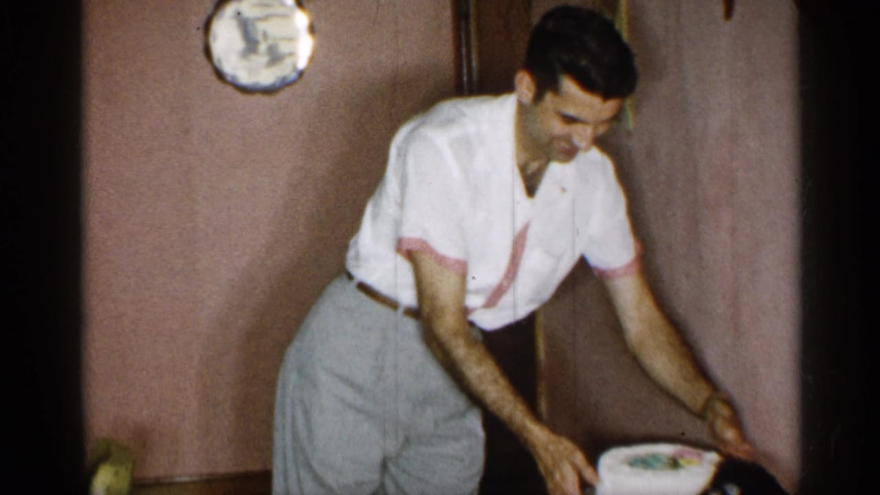 Man bends forward while setting a frosted cake on a table.