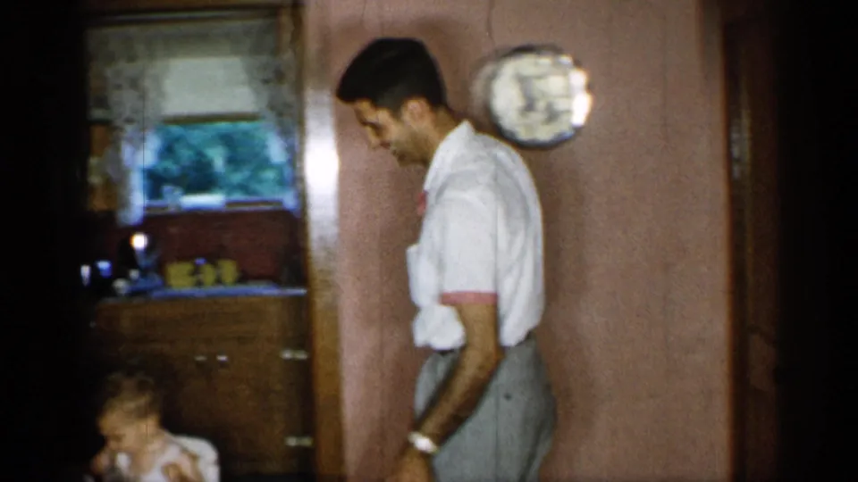 A side view shows the barefoot man moving beside the dining area while a young child sits low at the left of the frame.