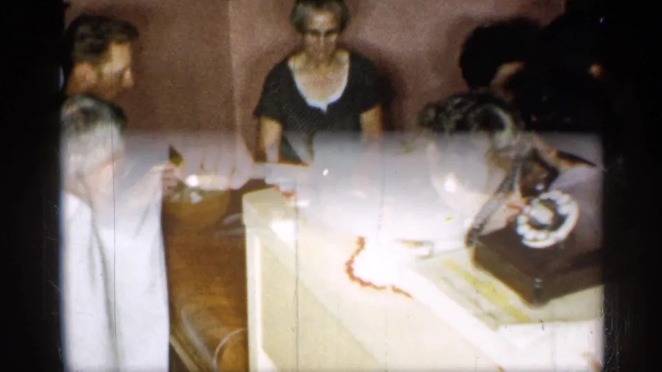 1955 New York home-movie frame with a frosted cake on a side table near a black rotary telephone.