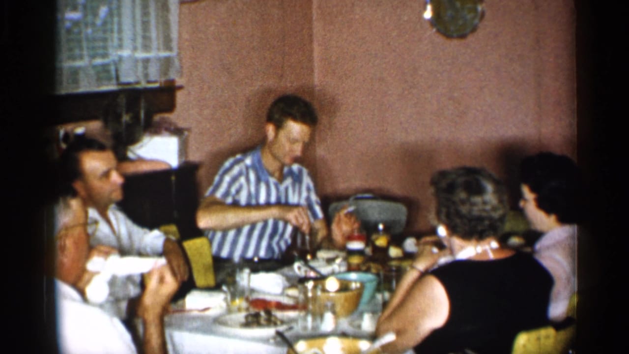 Home-movie view of adults eating and conversing around a dining table in a private New York interior, dated by metadata to 1955.