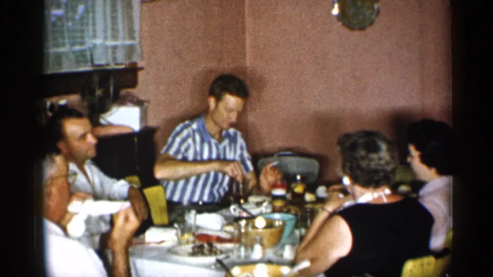 Home-movie view of adults eating and conversing around a dining table in a private New York interior, dated by metadata to 1955.