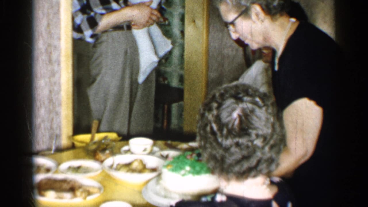 Woman in a black dress leans over a dinner table with a green-and-white cake and plates of food.