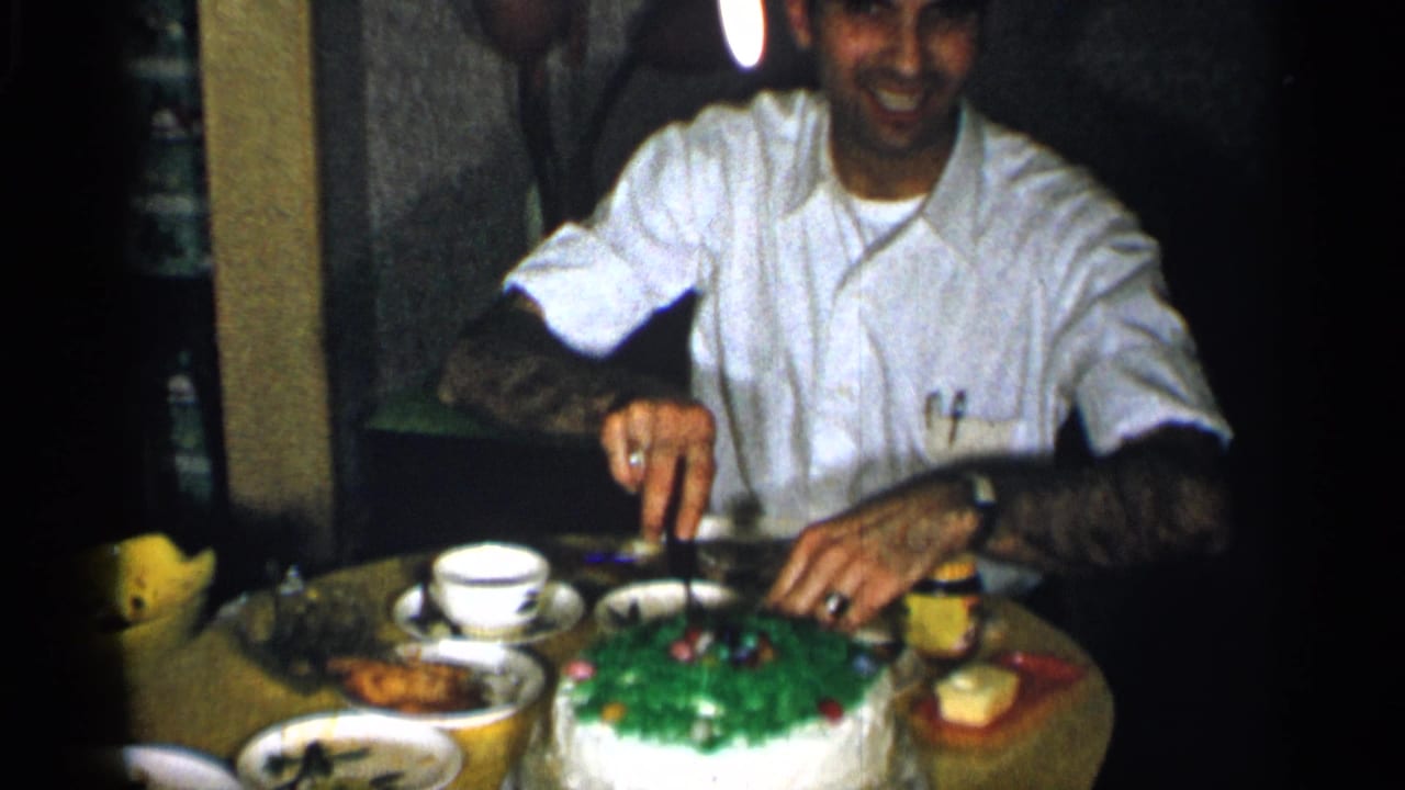 1955 New York home-movie frame showing a smiling man cutting a green-frosted cake during an indoor family meal.