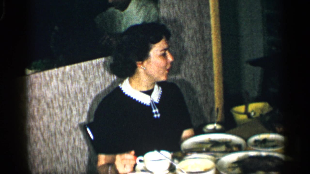 Woman in a black dress seated at a dining table with plates and cups.