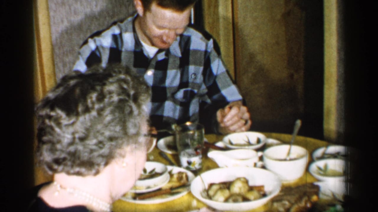 Adults seated at a crowded dining table with bowls, teacups, plates, and serving dishes.