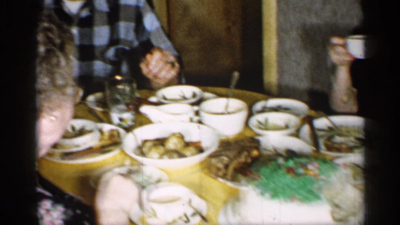 Dining table with adults, bowls, plates, teacups, and serving dishes in a home interior.