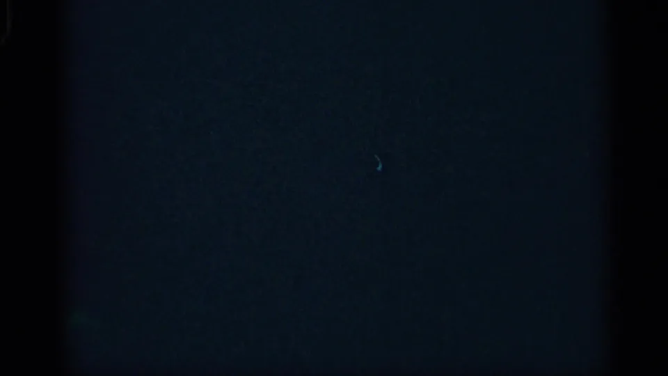 Mostly dark 8mm frame with faint bluish exposure, visible grain, and reel-edge shading, with no clear subject visible.
