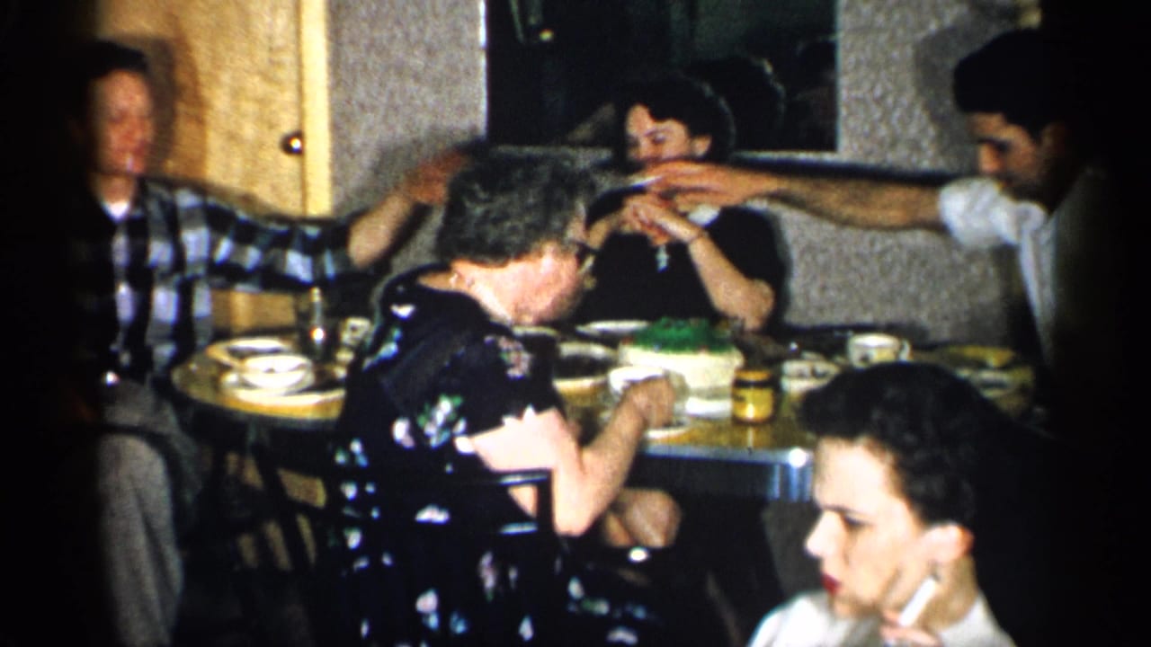Adults seated around a dinner table with dishes and a cake in a private interior.