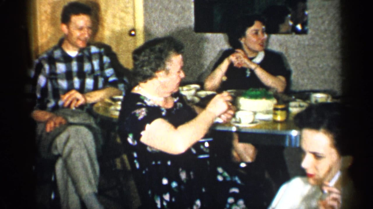 Adults seated around a restaurant table with cups, jars, and a dessert visible.