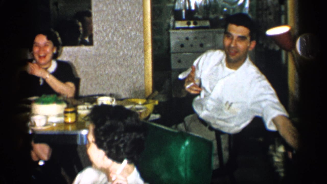 Adults seated at a restaurant table with a cake, cups, jars, and green booth seating.