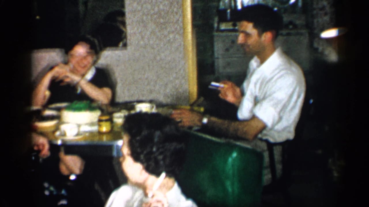 1955 New York restaurant scene with a man smoking at a table while women sit nearby around a cake and tableware.