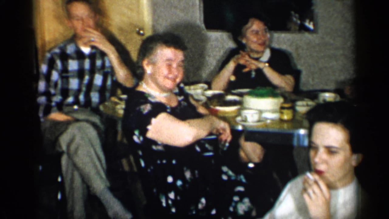 1955 New York restaurant gathering with adults seated around a table, a cake at center, and a woman in front eating or touching her mouth.