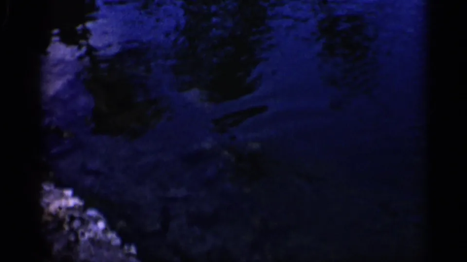 Dark blue-tinted 1958 Alabama 8mm frame showing rippled water and indistinct underwater fish or shadows.