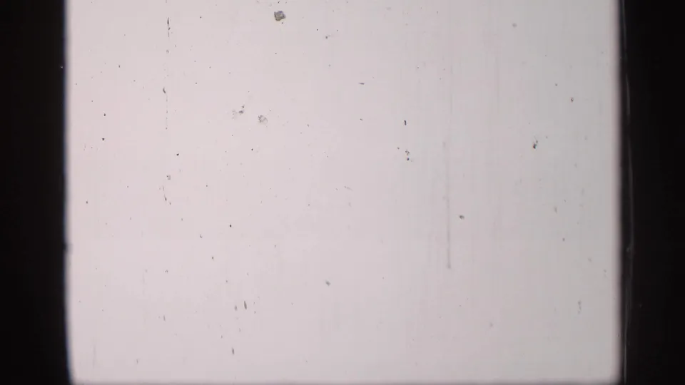 Pale overexposed 8mm frame with visible dust, scratches, and dark vertical borders, with little scene detail visible.