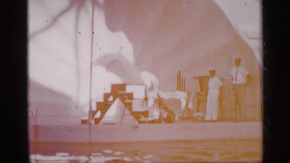 Faded 8mm frame from Alabama, 1958, showing a sea lion or seal act on red stairs near water and two handlers in white.