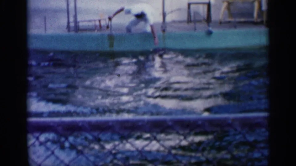 1958 Alabama home-movie frame showing a dolphin jumping in a pool near a white-uniformed trainer.