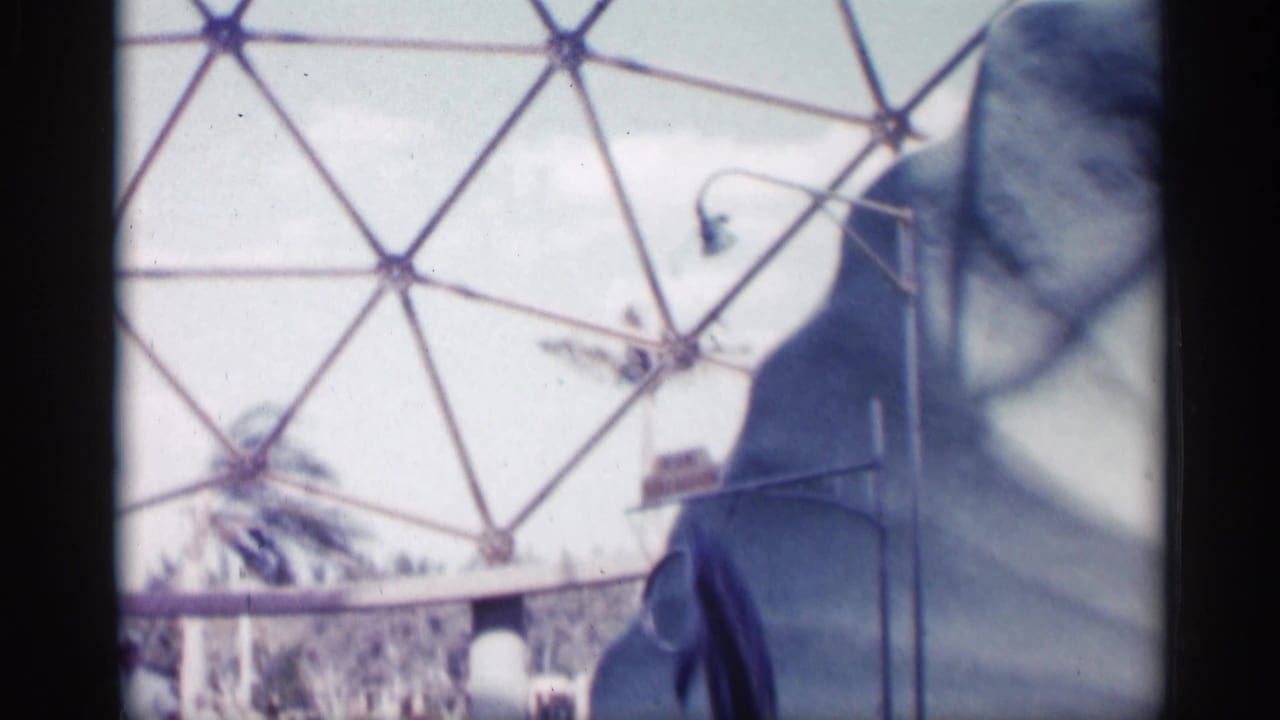 White-uniformed trainer stands near the pool area with a large geodesic dome frame behind the scene.