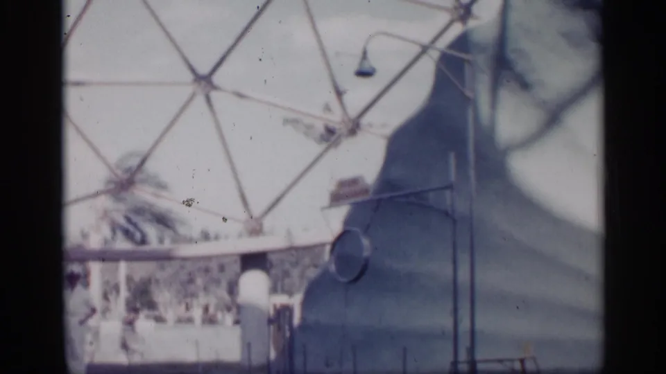 1958 Alabama home-movie frame showing a dolphin performance pool, a white-uniformed trainer, railings, and a large dome-like structure behind the show area.