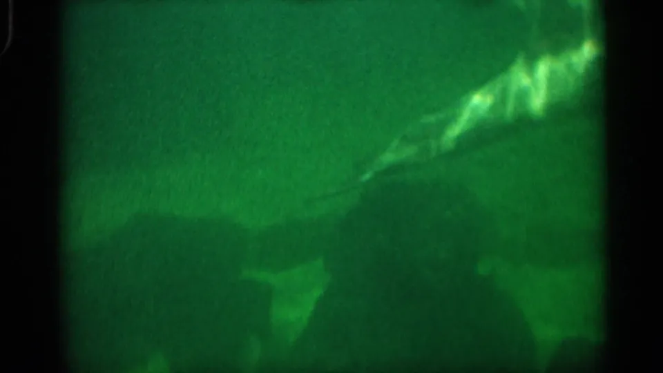 1958 Alabama 8mm frame showing a dolphin angled through green aquarium water, with dark silhouettes and soft underwater haze below.