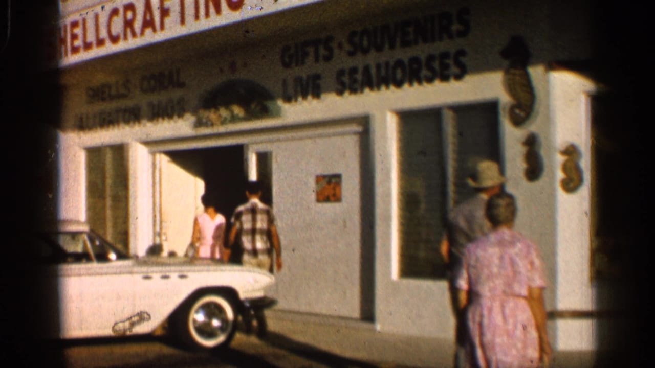 Tourists approach a shellcrafting souvenir shop beside a white convertible.