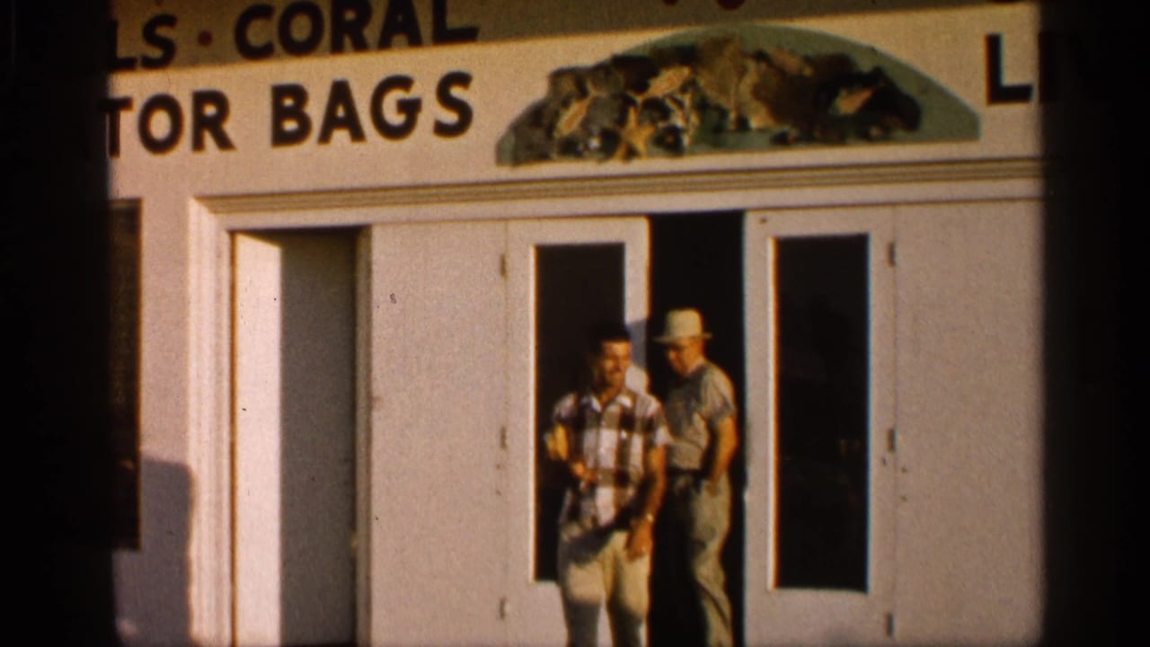 In 1958 Alabama footage, two men exit a storefront with glass-panel doors and a sign mentioning shells, coral, and bags.