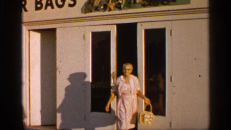 An older woman in a light patterned dress walks from the Alabama storefront, holding a handbag beside the glass-panel doors.