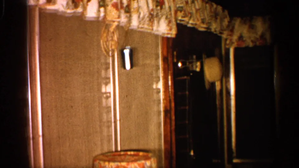 Interior view of a 1958 Alabama living-room corner with curtains, dark doorway or window, and a small table visible.