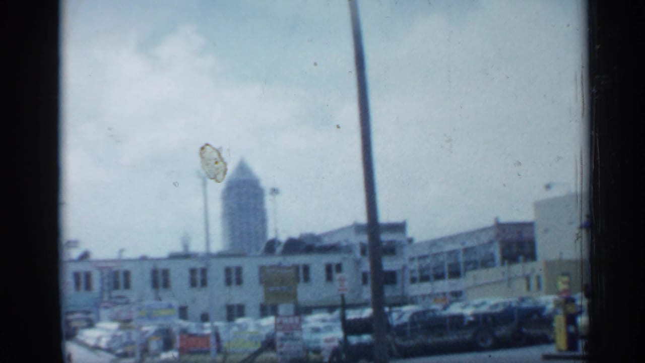 1958 Florida street scene showing parked cars, low commercial buildings, signage, utility poles, and a distant tower beyond the block.