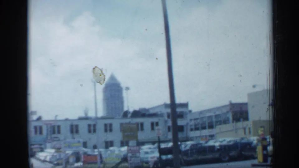 1958 Florida street scene showing parked cars, low commercial buildings, signage, utility poles, and a distant tower beyond the block.