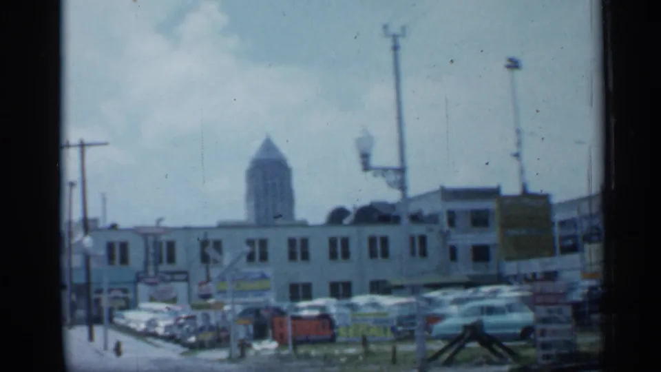 1958 Florida downtown view with a row of classic cars, commercial buildings, signs, utility poles, and a distant tower in soft focus.