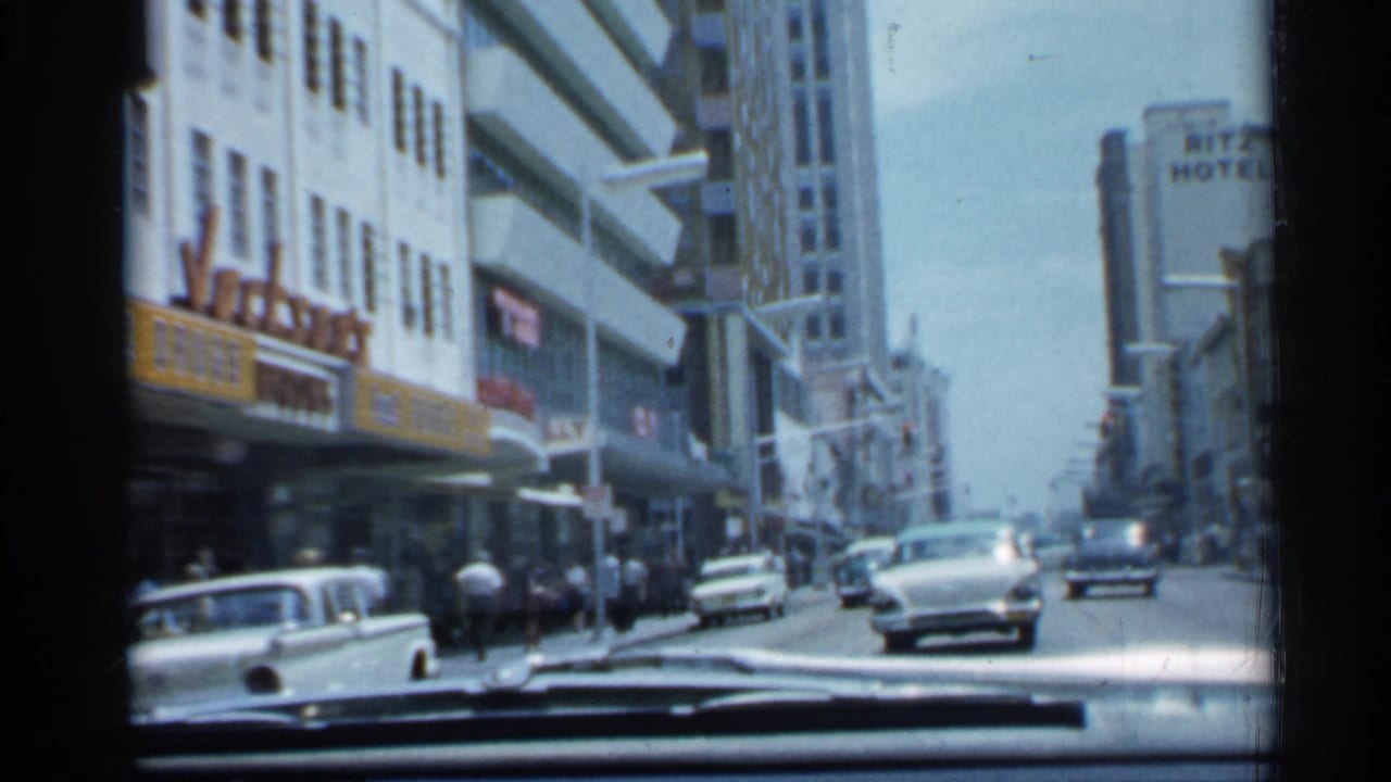 1958 Florida car-travel view down a commercial street with mid-century automobiles, pedestrians, storefronts, and a Ritz Hotel sign ahead.