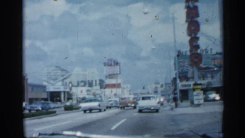 1958 Florida driving shot along a broad commercial street with late-1950s cars, storefront signage, and a prominent vertical Moo sign.