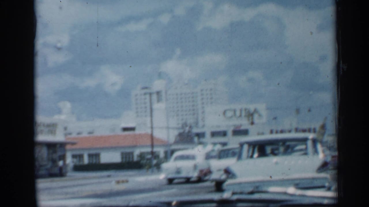 Roadside view with classic cars, a high-rise building, and a large Cuba sign on a commercial facade.