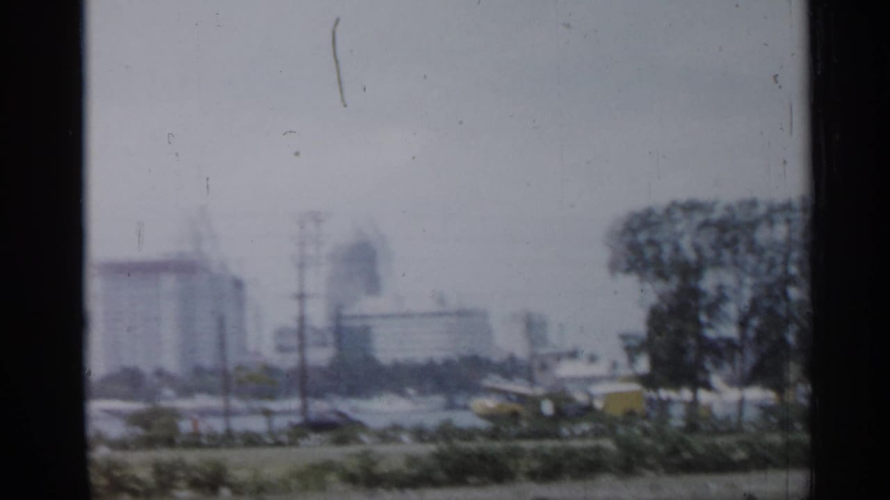 Hazy Florida city view with mid-century high-rises, utility poles, and roadside or waterfront foreground.