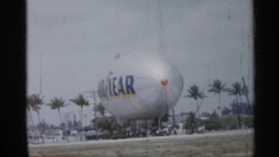A large Goodyear advertising balloon stands out in a 1958 Florida roadside city scene with palms and low buildings.