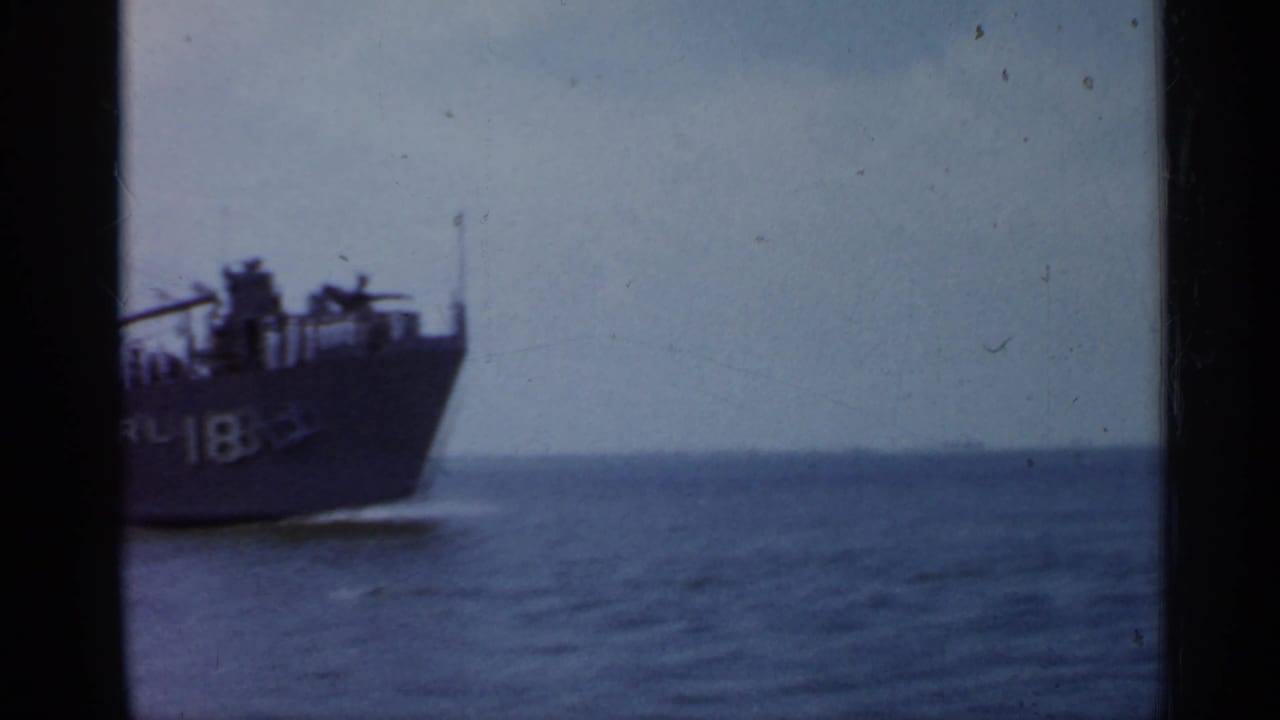 1958 Florida 8mm frame showing the bow of a large ship marked RL-18 passing on calm water, with film gate edges visible.