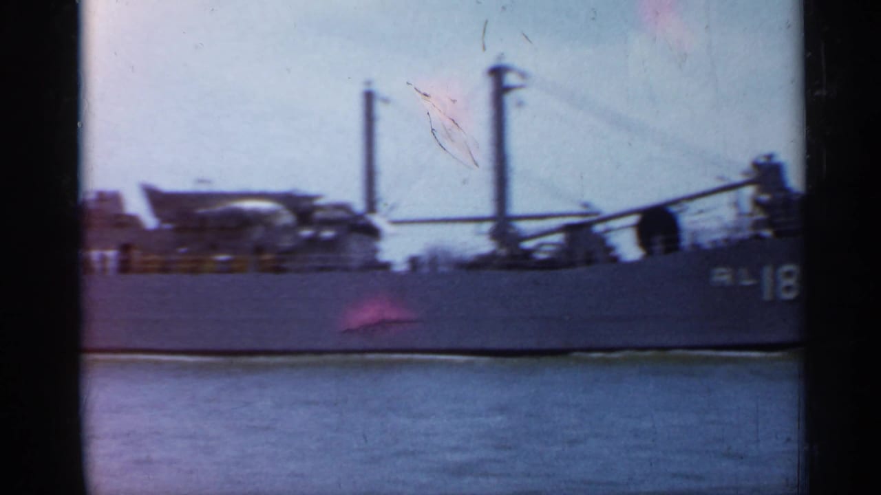 1958 Florida 8mm frame showing the side of the RL-18 vessel with deck structures, masts, and calm water in the foreground.