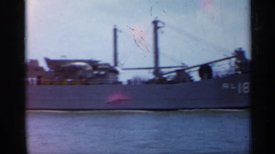 1958 Florida 8mm frame showing the side of the RL-18 vessel with deck structures, masts, and calm water in the foreground.