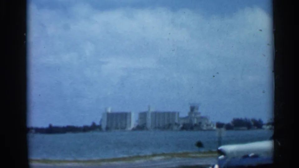 1958 Florida 8mm frame showing a distant waterfront skyline across calm water, with a partial boat edge at lower right.